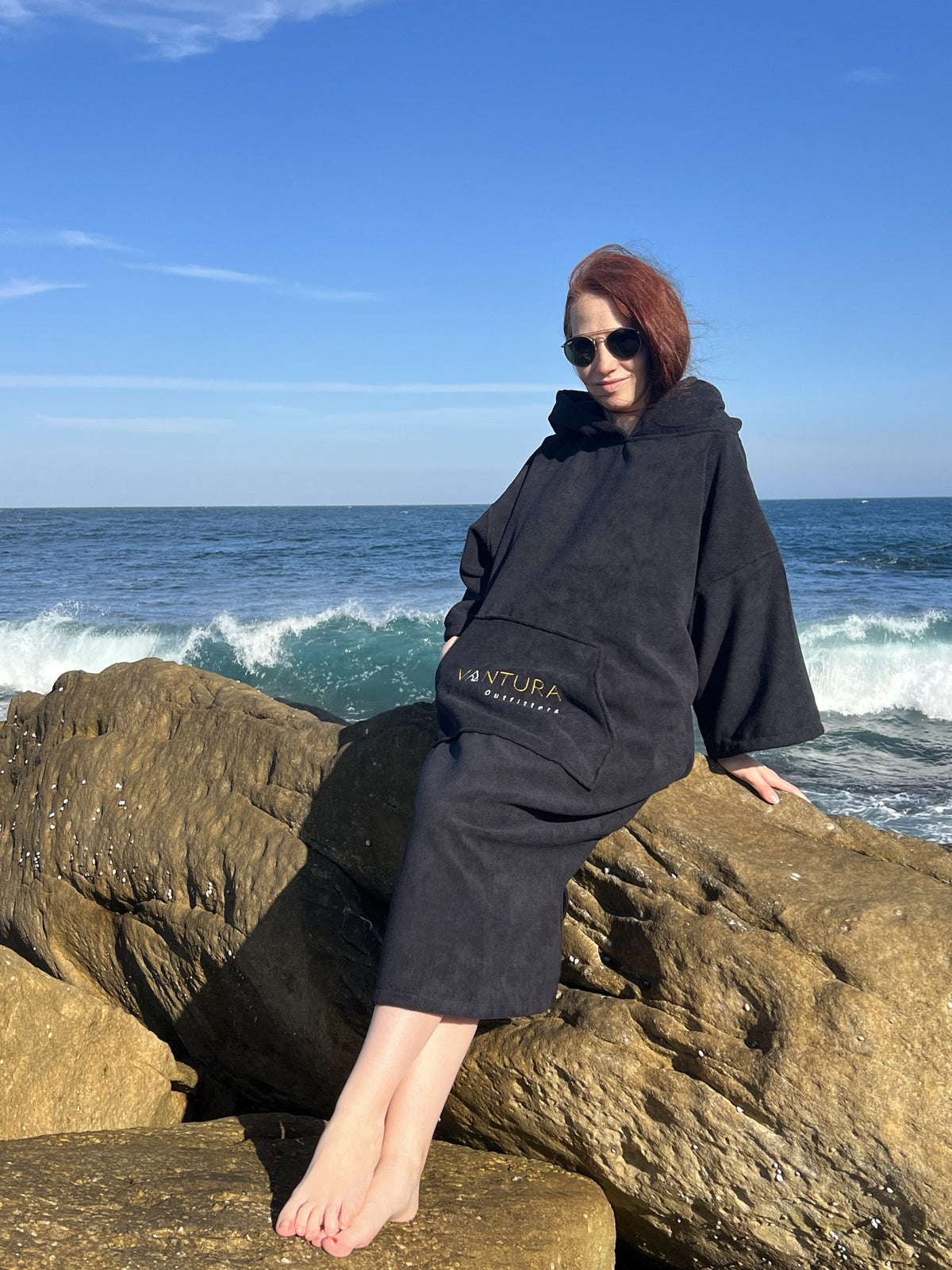 Woman seated on coastal rocks in the hooded changing poncho