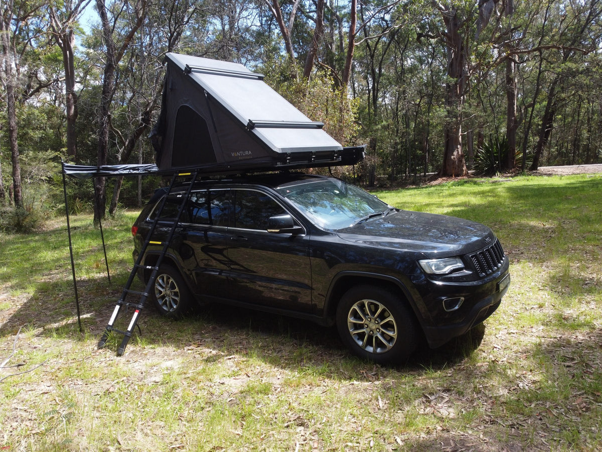 Vehicle with open rooftop tent, ladder and awning at camp